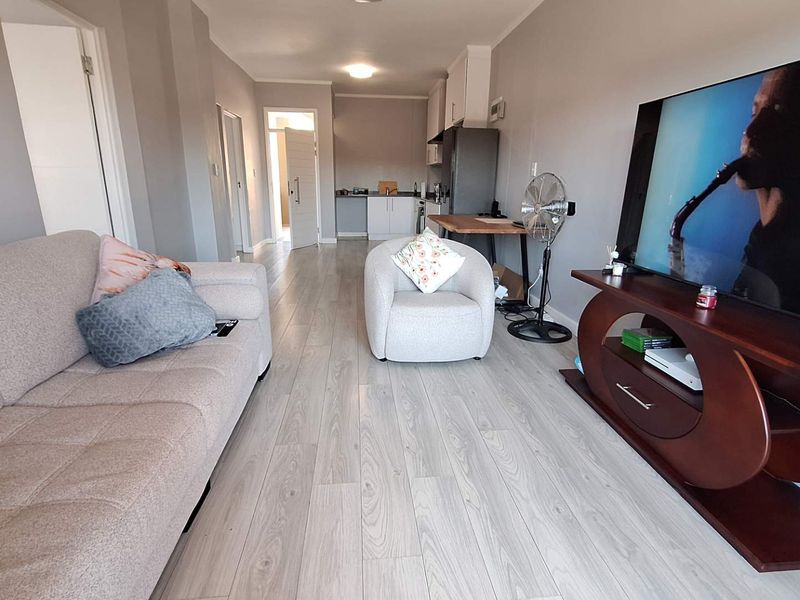 An open-plan living area featuring light-toned laminate flooring and a compact kitchen space visible in the background.