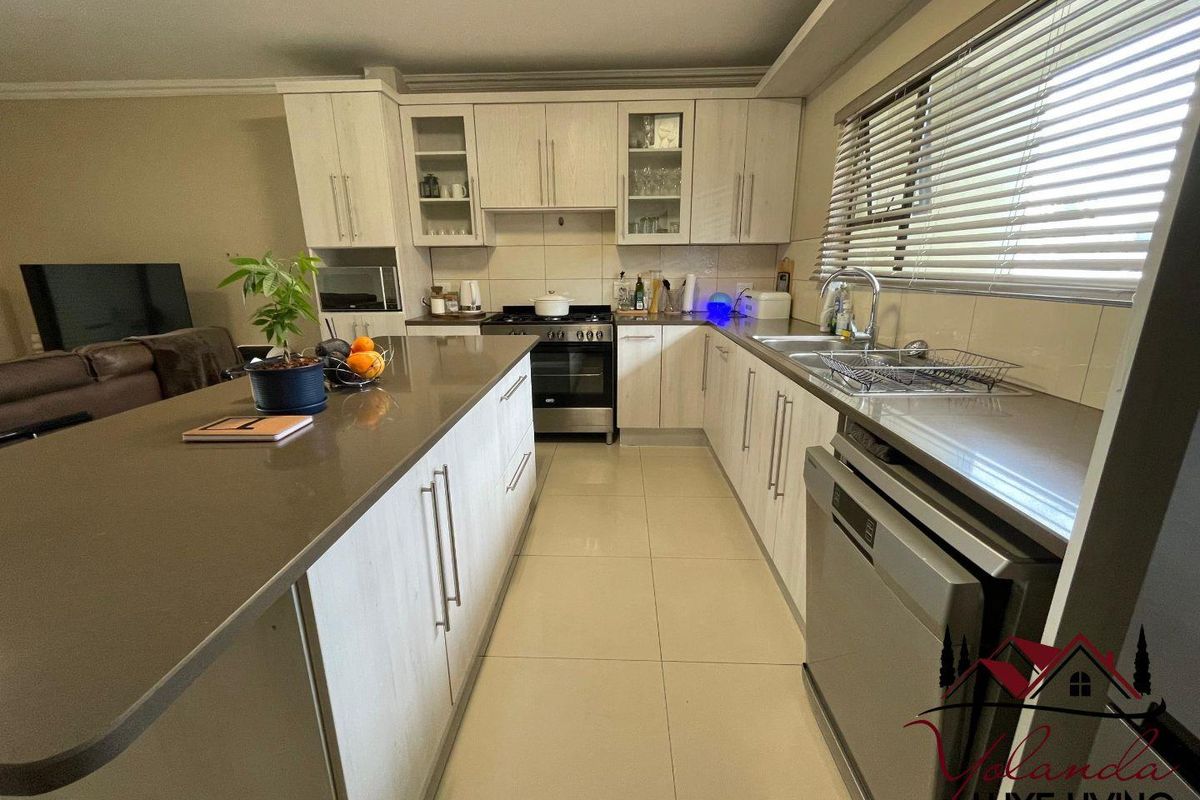 Modern kitchen featuring light wood-grain cabinetry, stone countertops, a central island, and stainless steel appliances, complemented by tiled flooring and natural light.