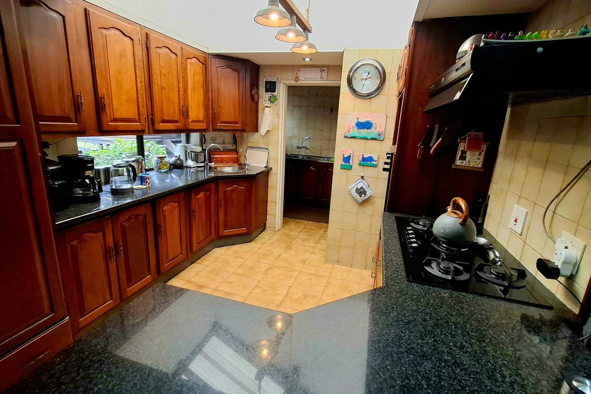 A functional kitchen featuring traditional wooden cabinetry, dark granite countertops, a gas hob with extractor fan, and tiled finishes throughout.
