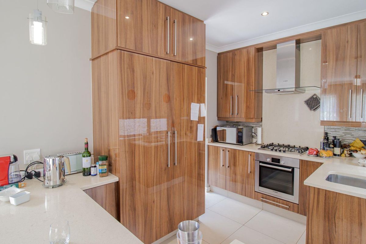 Modern kitchen featuring high-gloss wood cabinetry, stone countertops, integrated oven, gas hob, and stainless steel extractor fan.