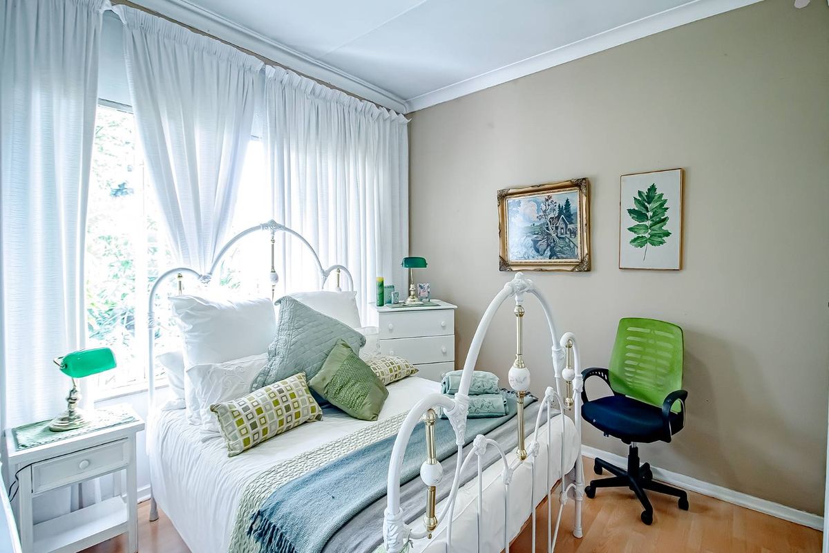 A well-maintained bedroom featuring laminate flooring, neutral wall tones, and large windows with curtain tracks.
