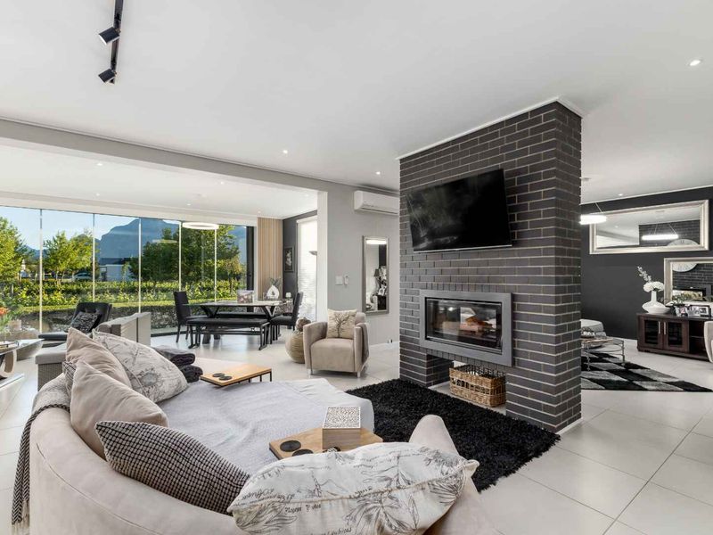 Spacious open-plan living area featuring a central brick fireplace, large glass sliding doors, and modern tiled flooring with recessed lighting.