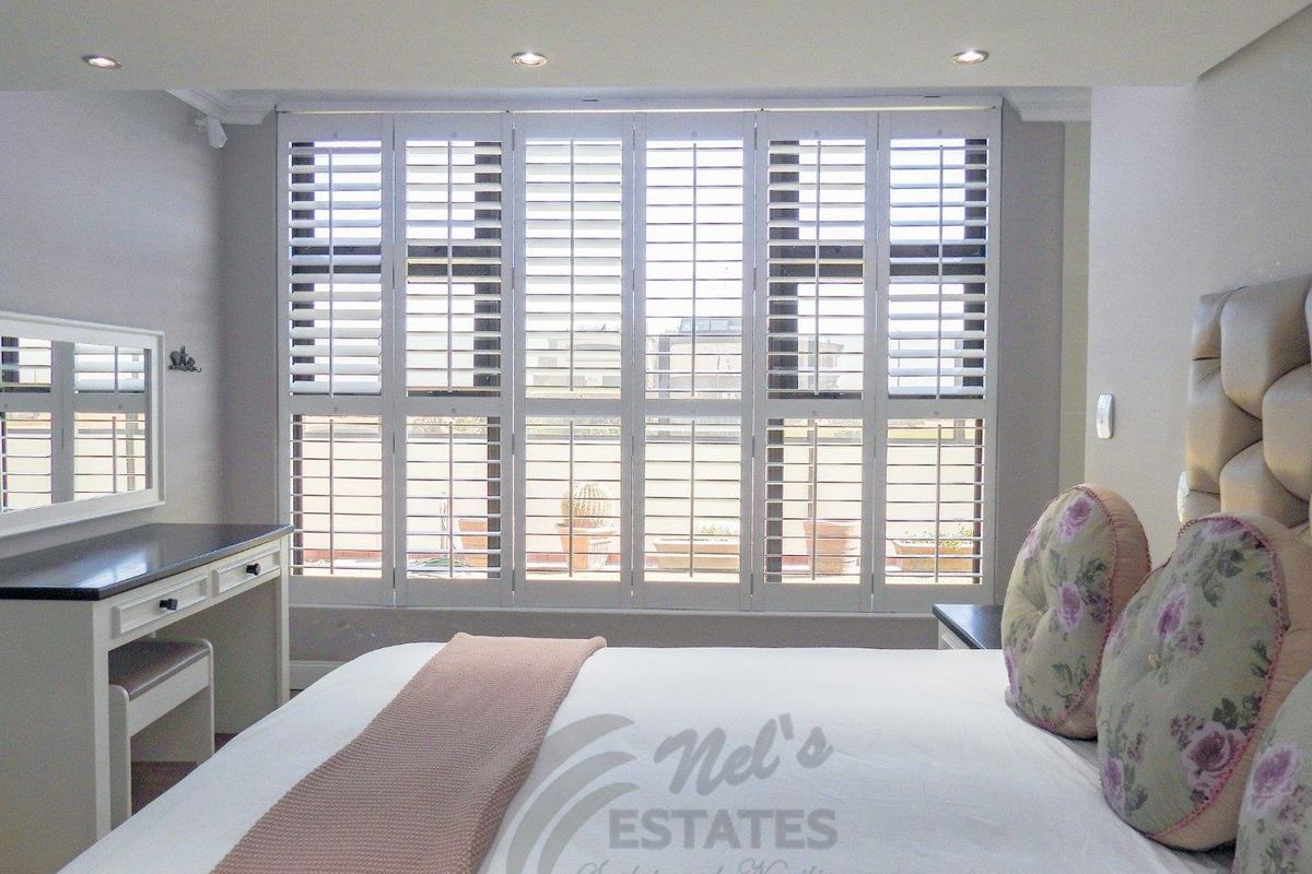 A well-maintained bedroom featuring large windows with fitted white plantation shutters and recessed ceiling lighting.