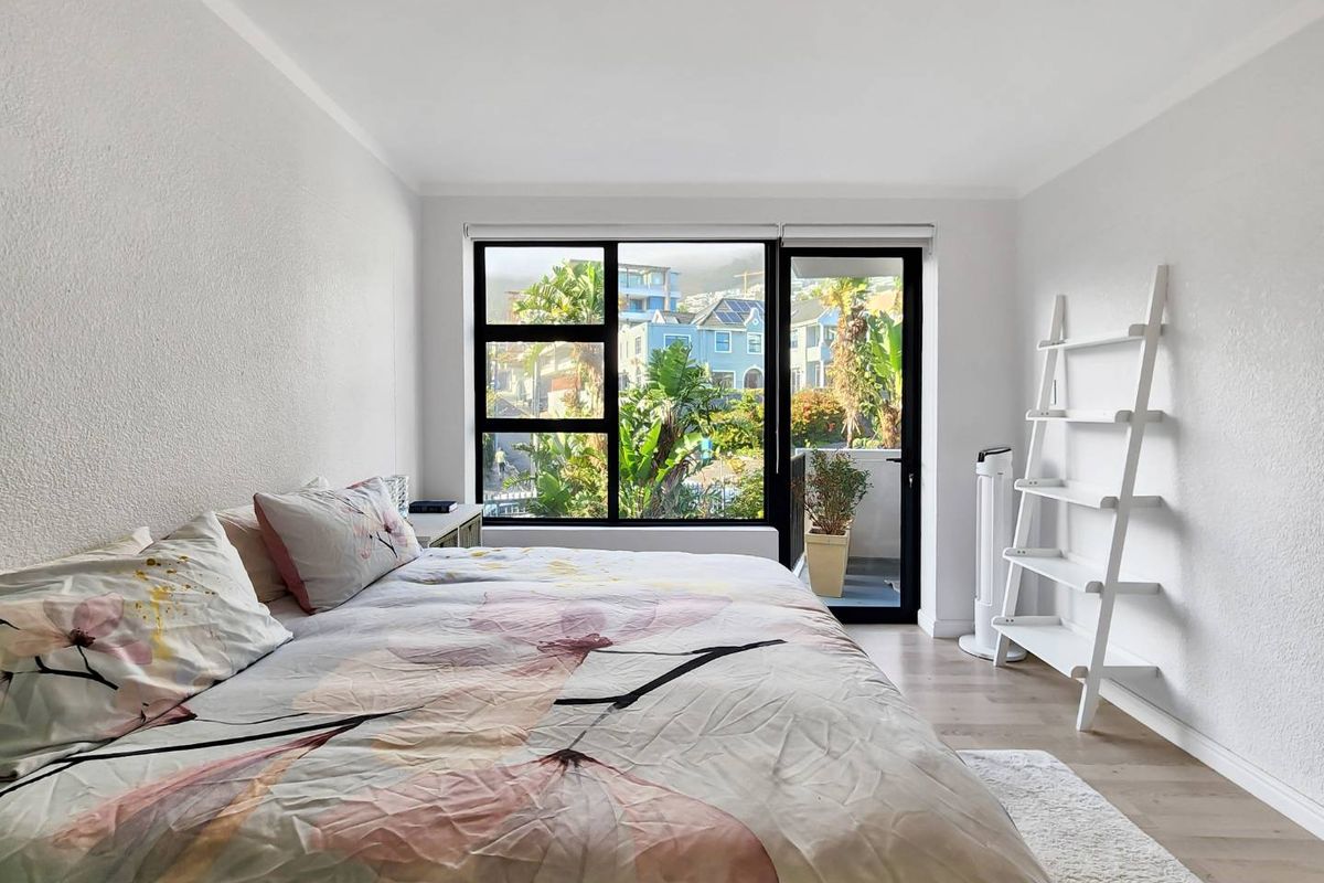 A bright and airy bedroom featuring laminate flooring, large windows providing natural light, and direct access to a private balcony.