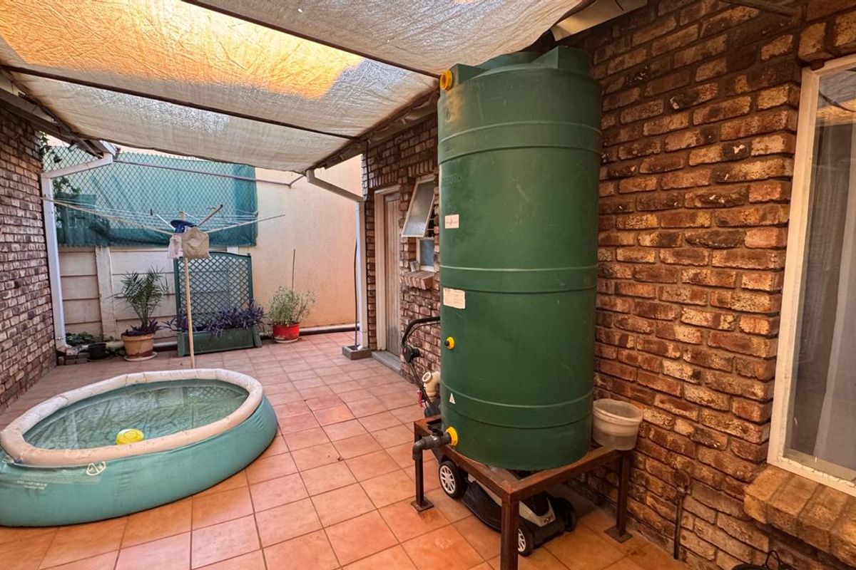 A paved rear patio area featuring a large water storage tank, brick wall finishes, and a covered outdoor space.