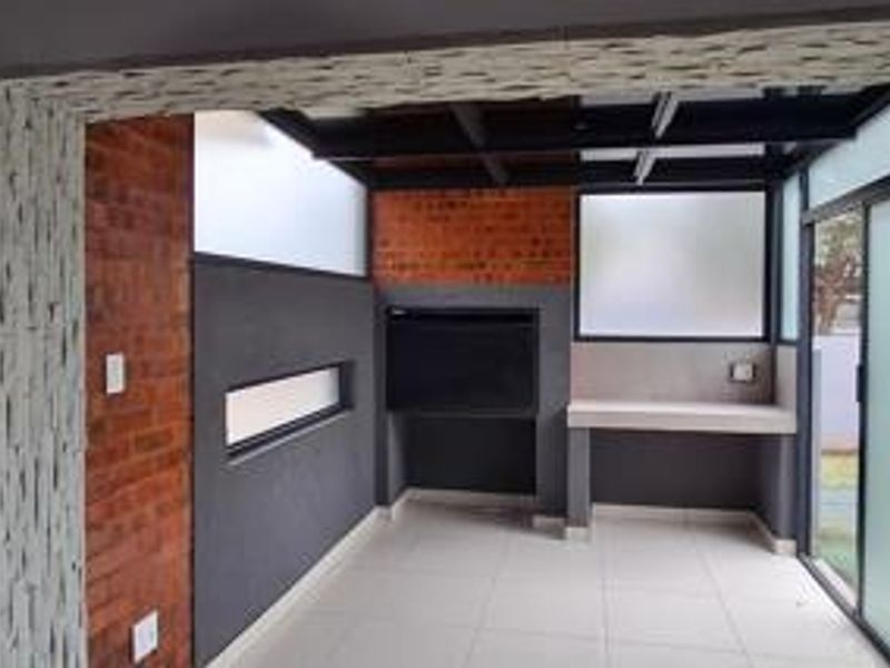 A modern covered patio area featuring a built-in braai, stone-clad accents, exposed ceiling beams, and tiled flooring, perfect for outdoor entertaining.