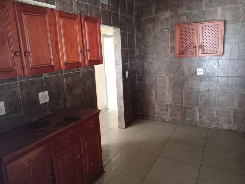 A dated kitchen featuring dark tiled walls and wooden cabinetry, offering a blank canvas for potential modern renovation and aesthetic updates.
