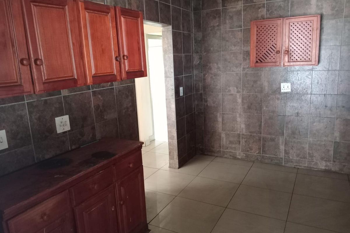 A dated kitchen featuring dark tiled walls and wooden cabinetry, offering a blank canvas for potential modern renovation and aesthetic updates.