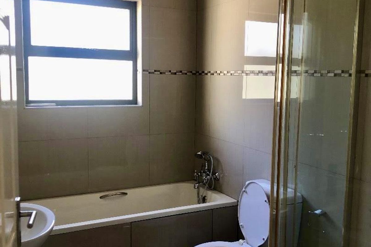 A functional bathroom featuring a built-in bathtub, a separate glass-enclosed shower, and a standard toilet with neutral wall and floor tiling.