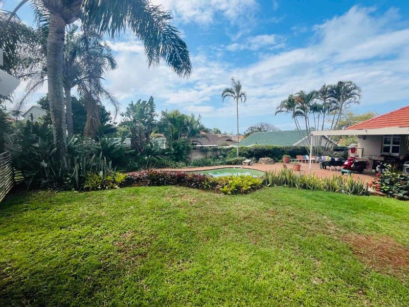 A spacious backyard featuring a swimming pool, paved patio area, and established garden landscaping, ideal for outdoor relaxation and entertainment.