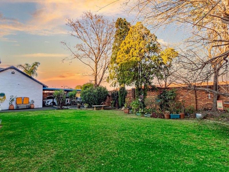A spacious rear garden featuring a well-maintained lawn, brick boundary wall, and an attached carport area.