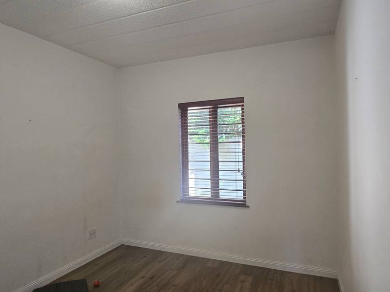 A clean, empty bedroom featuring laminate flooring, neutral walls, and window blinds, providing a blank canvas for personalization.
