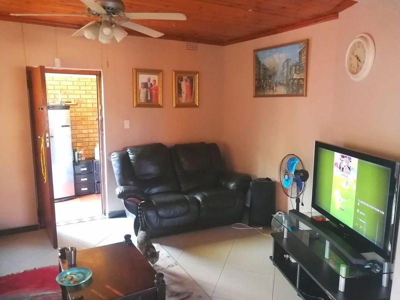 A living room featuring a timber ceiling, ceiling fan, and tiled flooring, with an adjacent doorway leading to a utility area.