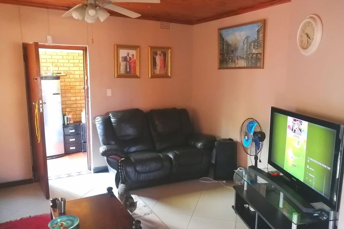 A living room featuring a timber ceiling, ceiling fan, and tiled flooring, with an adjacent doorway leading to a utility area.