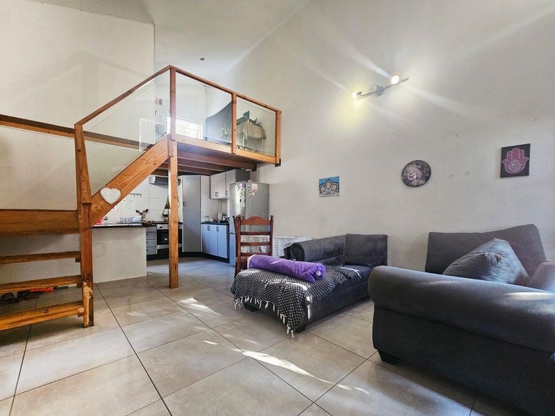 Open-plan living area featuring a mezzanine level with timber staircase, glass balustrade, and an integrated kitchen with built-in cabinetry and appliances.