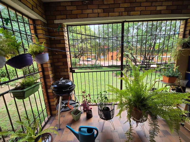 Covered patio area featuring brick walls, tiled flooring, and security bars, overlooking a communal garden space.