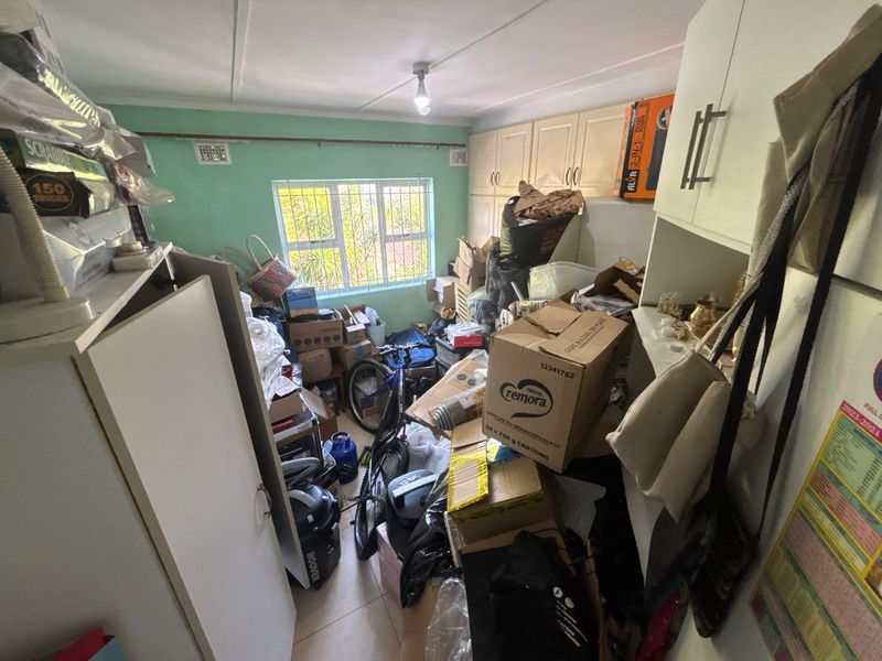 A bedroom featuring built-in cupboards, tiled flooring, and security bars on the window, currently used for storage.