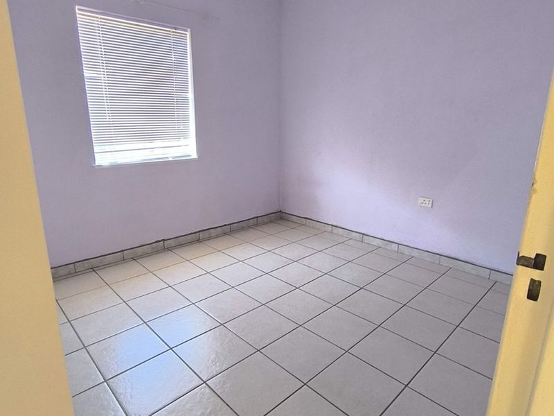 A clean, empty bedroom featuring neutral tiled flooring, light-colored walls, and fitted venetian blinds, offering a blank canvas for personalization.