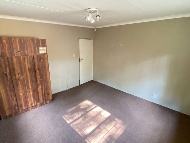 A bedroom featuring carpeted flooring, a built-in wooden wardrobe, and neutral wall tones, offering a functional space ready for personalization.