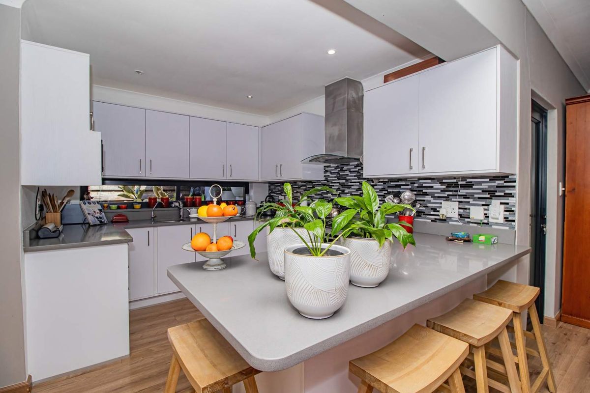 Modern kitchen featuring white cabinetry, stone countertops, a breakfast bar, and a mosaic tile backsplash with a stainless steel extractor fan.