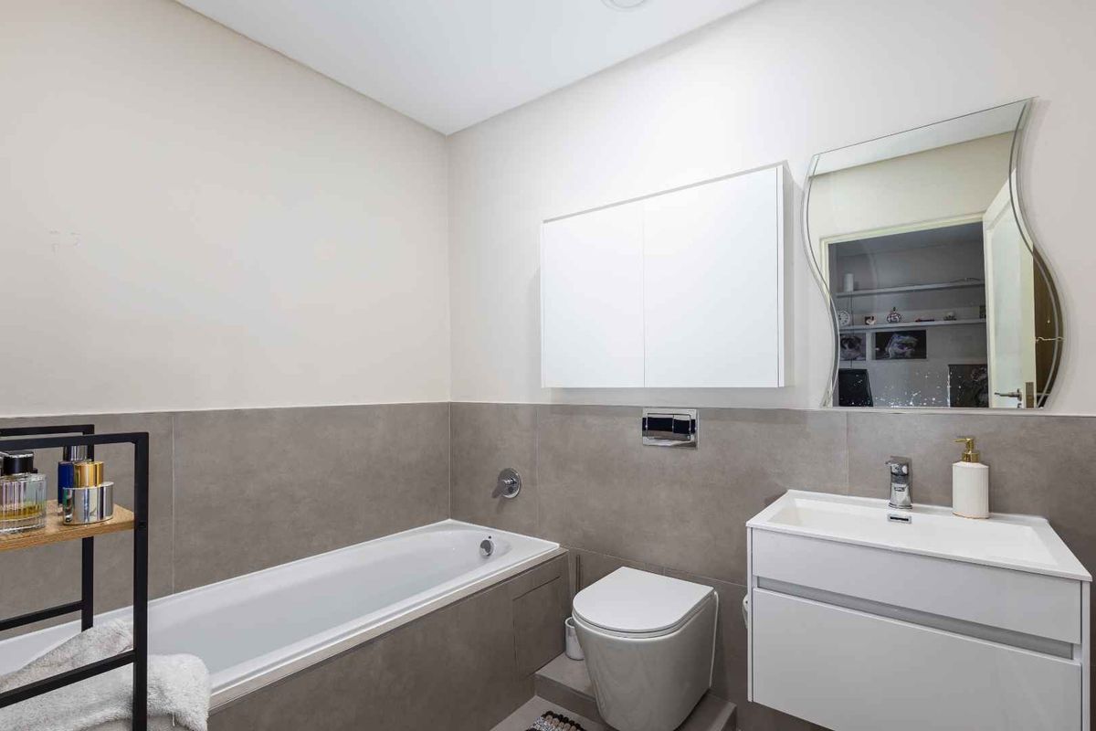 Modern bathroom featuring a built-in bathtub, wall-mounted toilet, vanity cabinet with basin, and a wall-mounted medicine cabinet with neutral tiling.