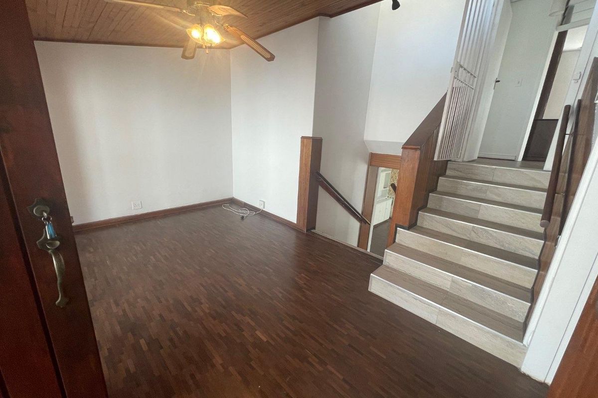 An empty living area featuring parquet flooring, a timber ceiling with a ceiling fan, and a staircase leading to the upper level.