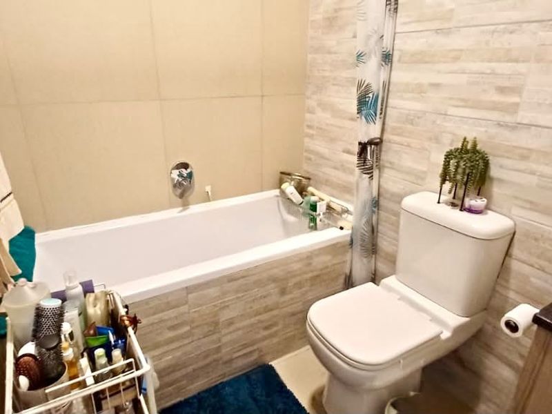 A compact bathroom featuring a bathtub, toilet, and vanity basin with neutral wall tiling.