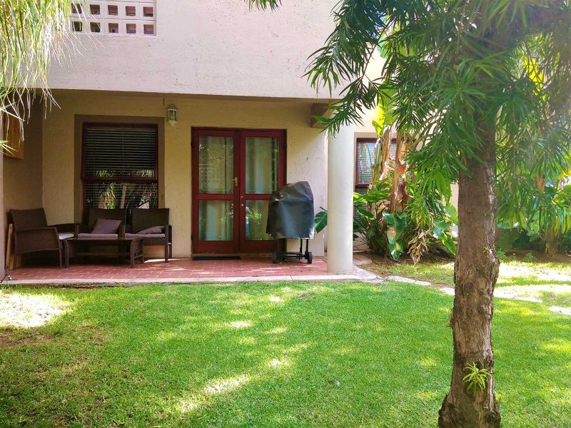 A rear view of the townhouse featuring a covered terracotta tiled patio, double glass doors, and a well-maintained private garden area.