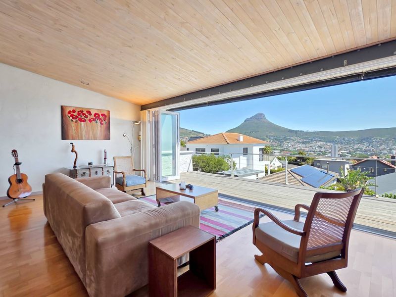 Spacious living area featuring hardwood floors, a timber-clad ceiling, and seamless indoor-outdoor flow to a deck with panoramic mountain and city views.
