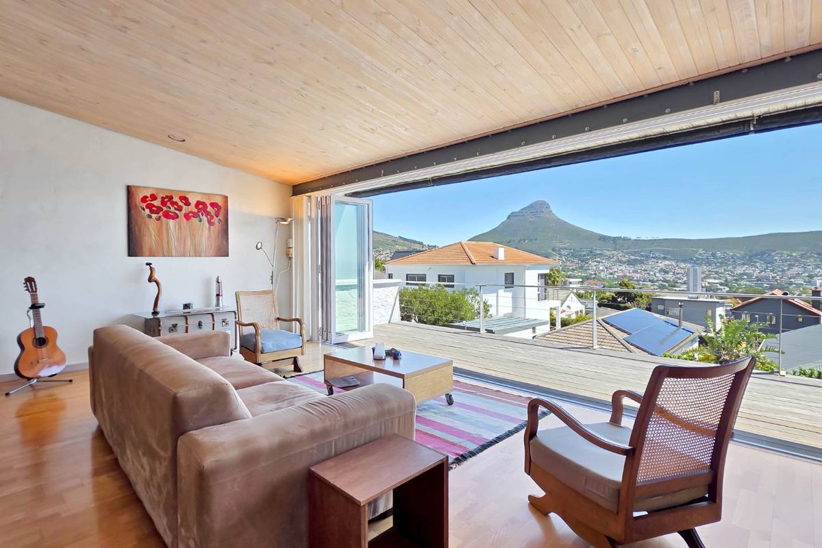 Spacious living area featuring hardwood floors, a timber-clad ceiling, and seamless indoor-outdoor flow to a deck with panoramic mountain and city views.