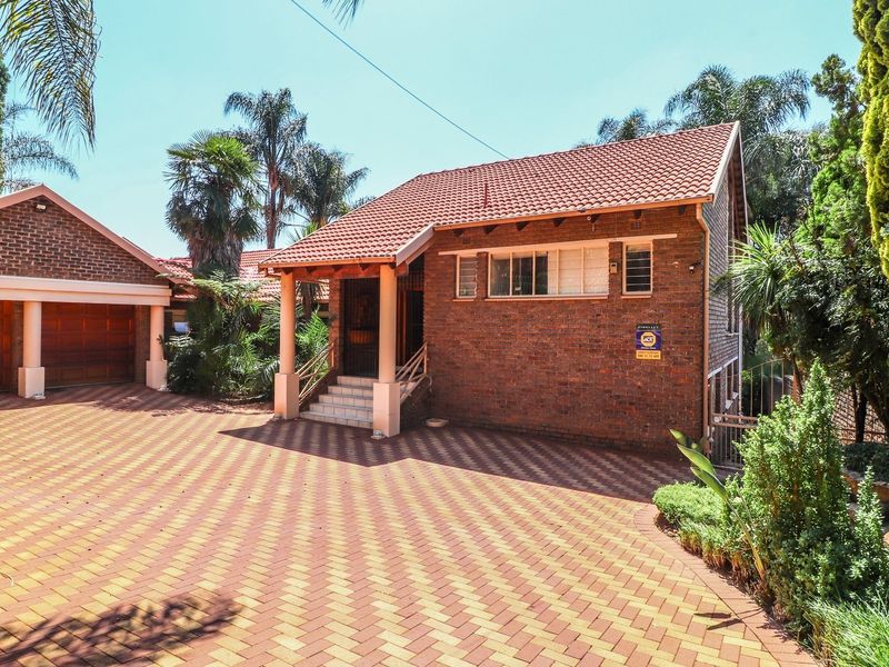 Front view of a well-maintained brick house featuring a spacious paved driveway, double garage, and a covered entrance porch.
