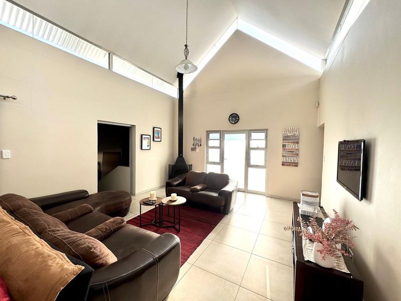 Spacious living room featuring a high vaulted ceiling with clerestory windows, tiled flooring, and a modern freestanding fireplace.