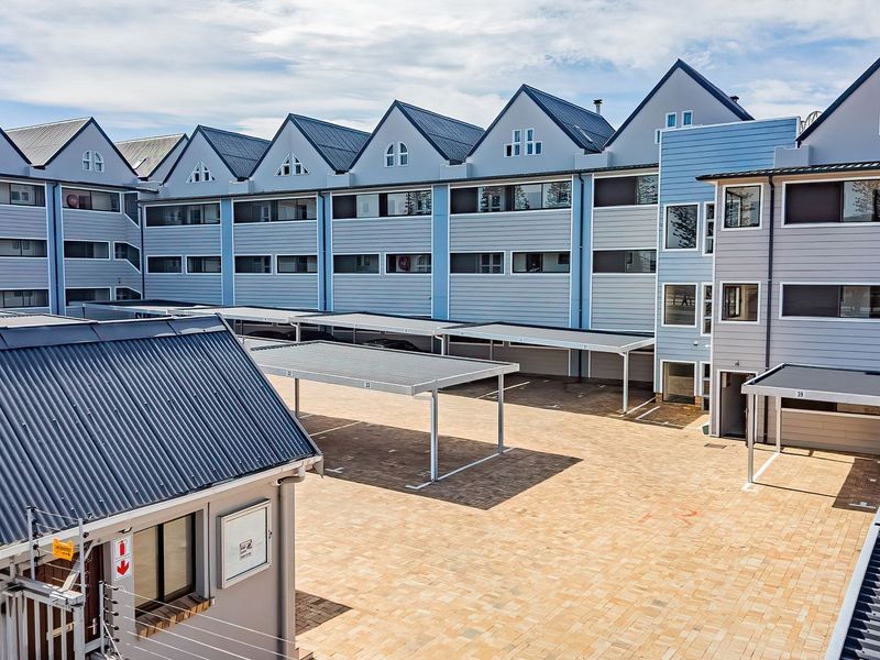 An elevated view of the apartment complex courtyard featuring paved parking areas, covered carports, and a secure entrance gatehouse.
