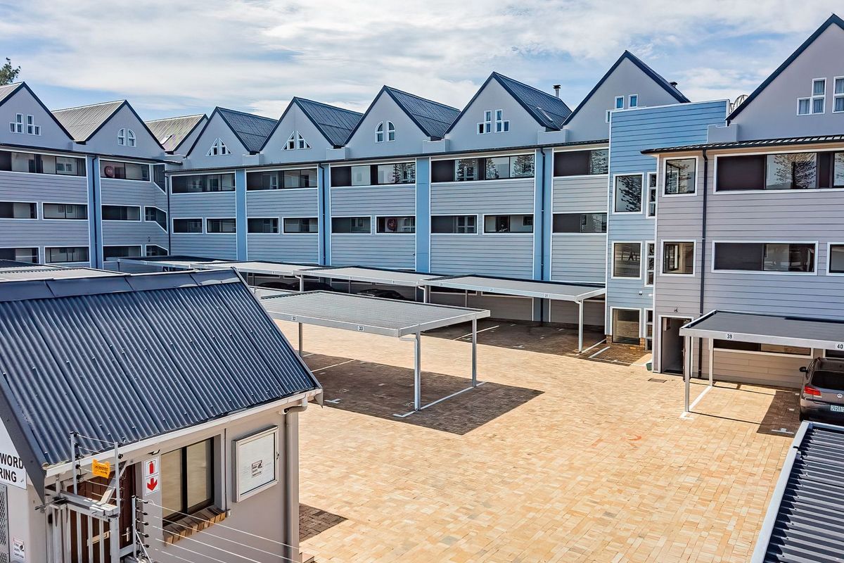 An elevated view of the apartment complex courtyard featuring paved parking areas, covered carports, and a secure entrance gatehouse.