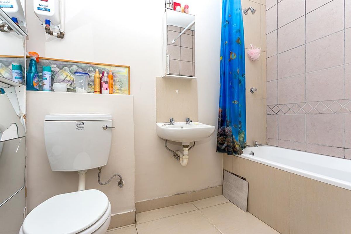 A functional bathroom featuring a bathtub with shower, wall-mounted basin, and toilet, requiring some cosmetic updates and repairs to fixtures.