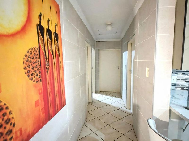 A clean, tiled hallway providing access to multiple rooms, featuring neutral wall tiles and a tiled floor.
