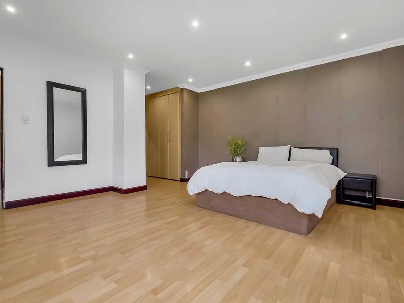 Spacious bedroom featuring light laminate flooring, recessed downlighting, and built-in cupboards with a neutral color palette.