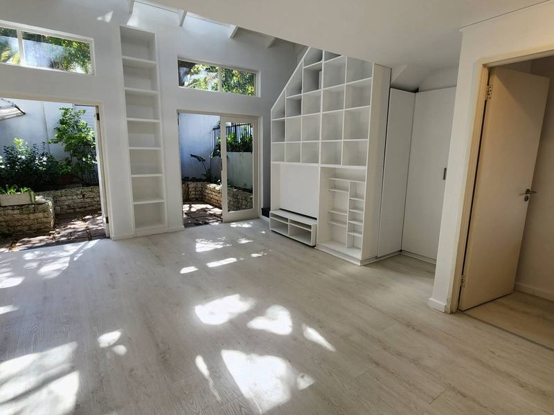 Bright and airy living room featuring light laminate flooring, extensive built-in shelving, and large glass sliding doors providing direct access to a private courtyard.