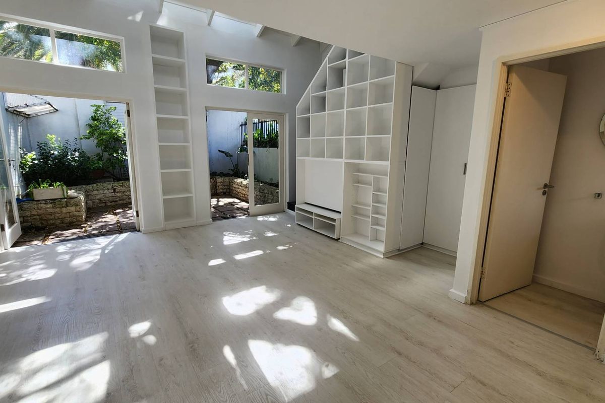 Bright and airy living room featuring light laminate flooring, extensive built-in shelving, and large glass sliding doors providing direct access to a private courtyard.