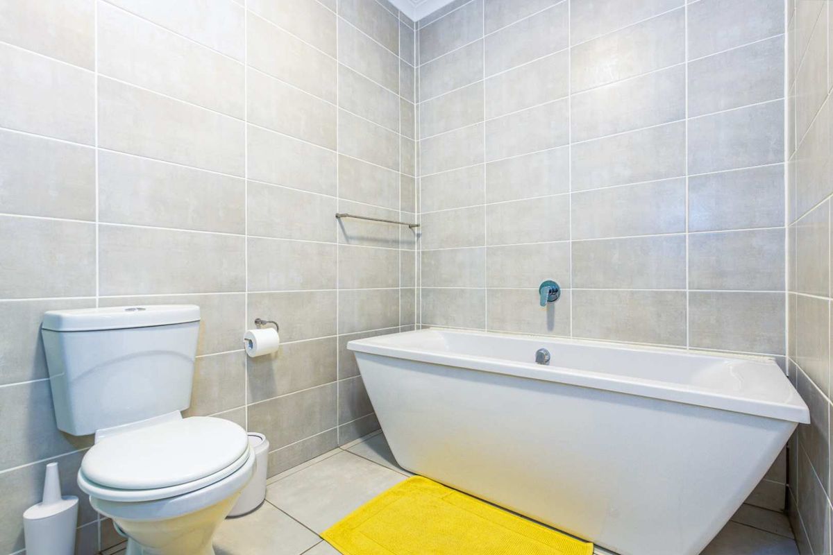 A modern bathroom featuring full-height wall tiling, a contemporary freestanding bathtub, and a standard toilet suite.