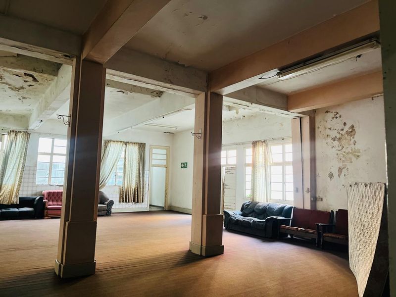 Spacious open-plan living area featuring structural columns and large windows, currently requiring significant renovation and cosmetic repairs to restore the interior finishes.