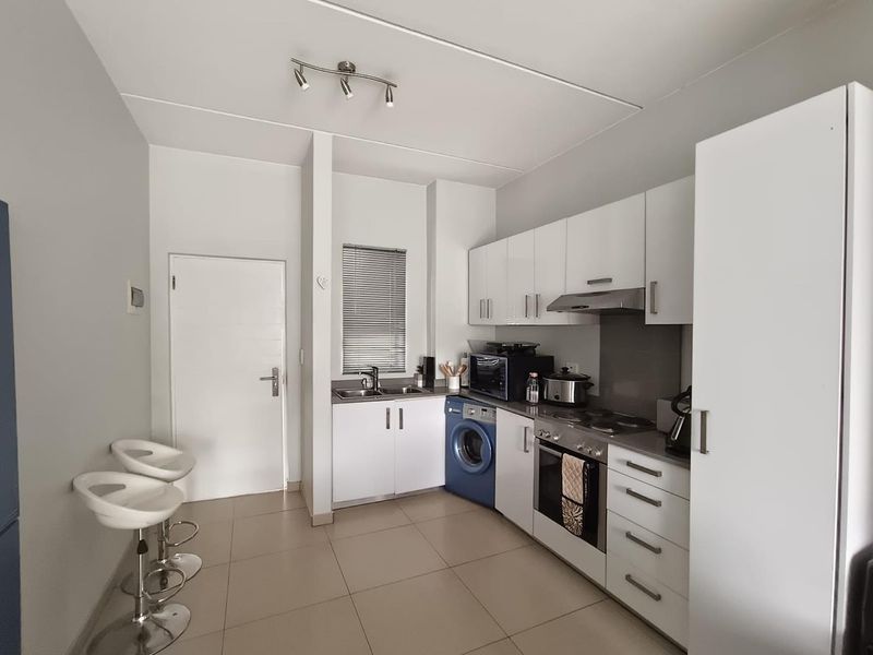 A functional kitchen featuring white cabinetry, integrated appliances, tiled flooring, and a stainless steel sink with a window view.