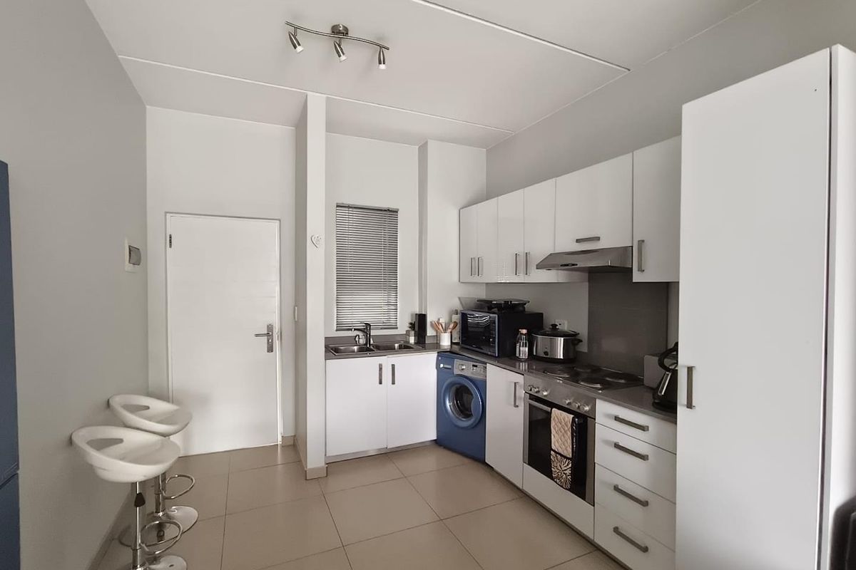 A functional kitchen featuring white cabinetry, integrated appliances, tiled flooring, and a stainless steel sink with a window view.