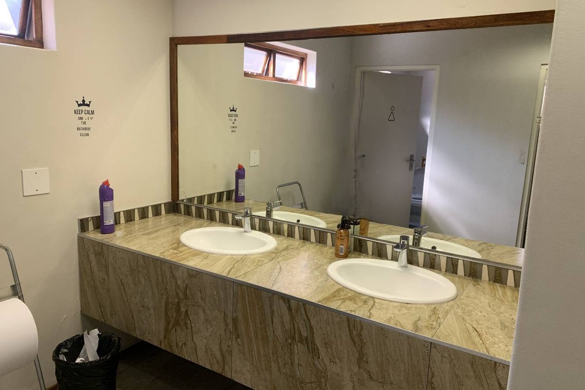 A functional office bathroom featuring a double vanity with drop-in sinks, tiled countertop, and a large wall-mounted mirror.