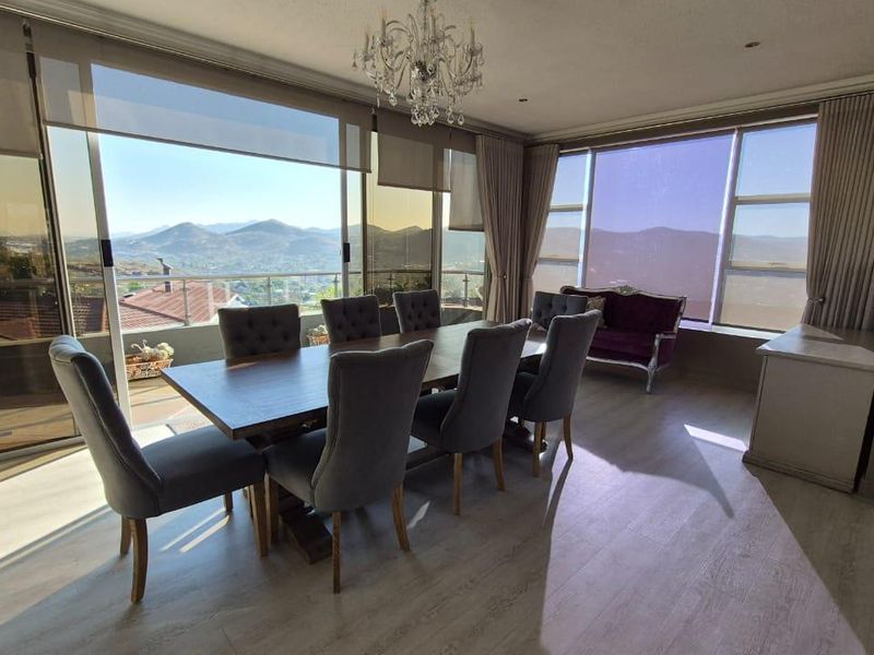 A bright and spacious dining room featuring large windows with panoramic mountain views, modern laminate flooring, and an elegant crystal chandelier.