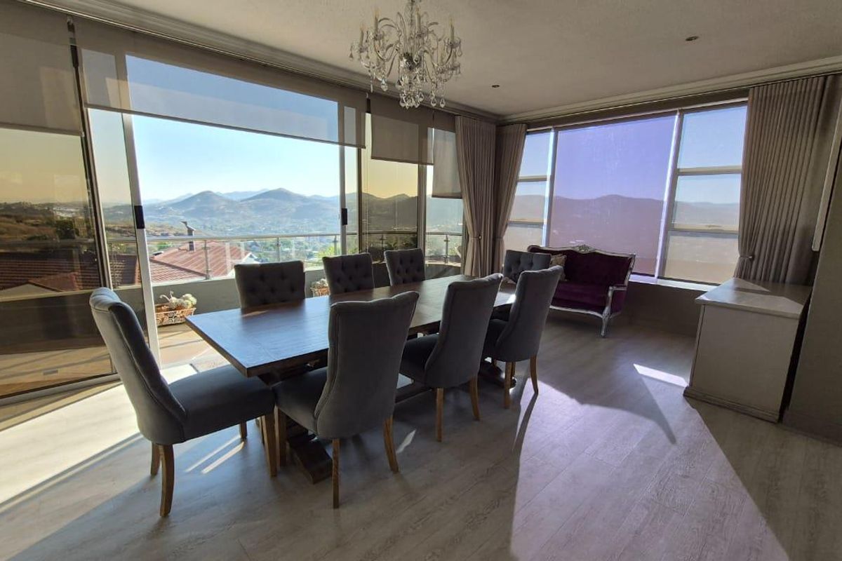 A bright and spacious dining room featuring large windows with panoramic mountain views, modern laminate flooring, and an elegant crystal chandelier.