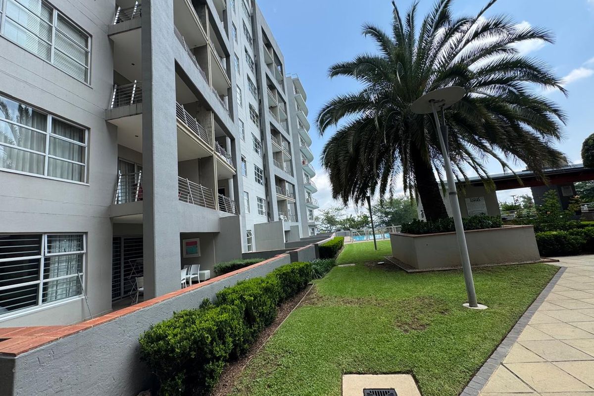 A view of the apartment building exterior featuring private balconies, well-maintained landscaped gardens, and paved walkways.