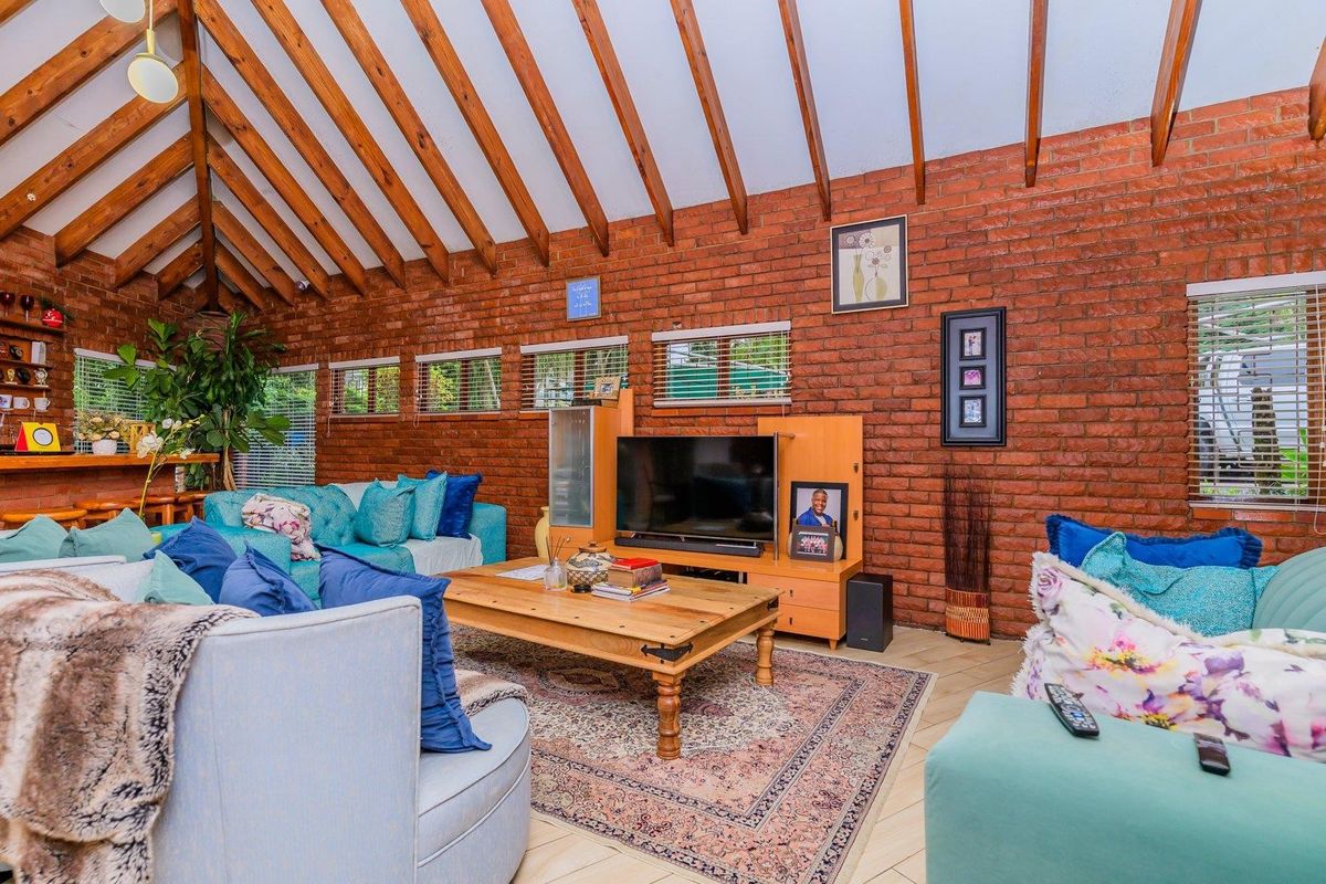 Spacious living room featuring high vaulted ceilings with exposed timber rafters, rustic exposed brick walls, and tiled flooring.
