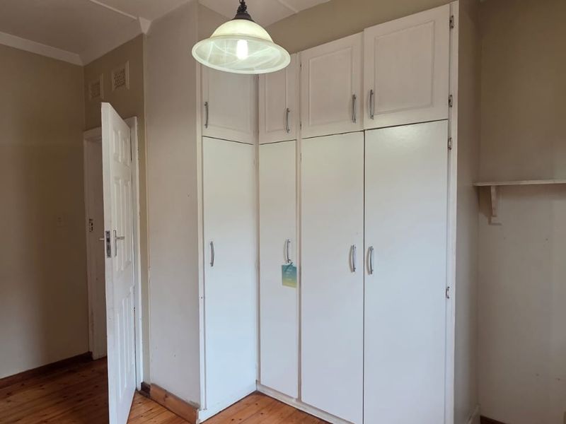 A vacant bedroom featuring timber flooring, built-in white cupboards, and a wall-mounted shelf, offering a blank canvas for personalization.