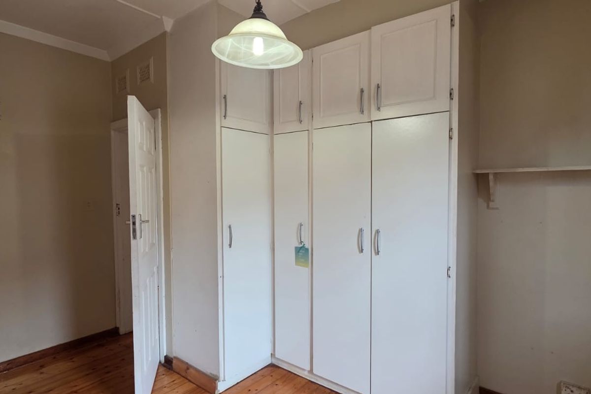 A vacant bedroom featuring timber flooring, built-in white cupboards, and a wall-mounted shelf, offering a blank canvas for personalization.